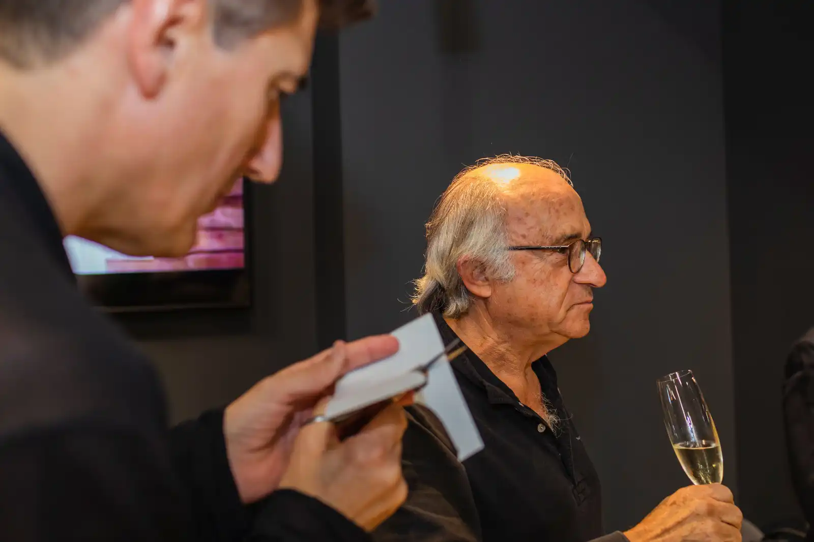 Um convidado com uma taça de champanhe enquanto Igor Kucinic recorta um retrato em silhueta num cocktail